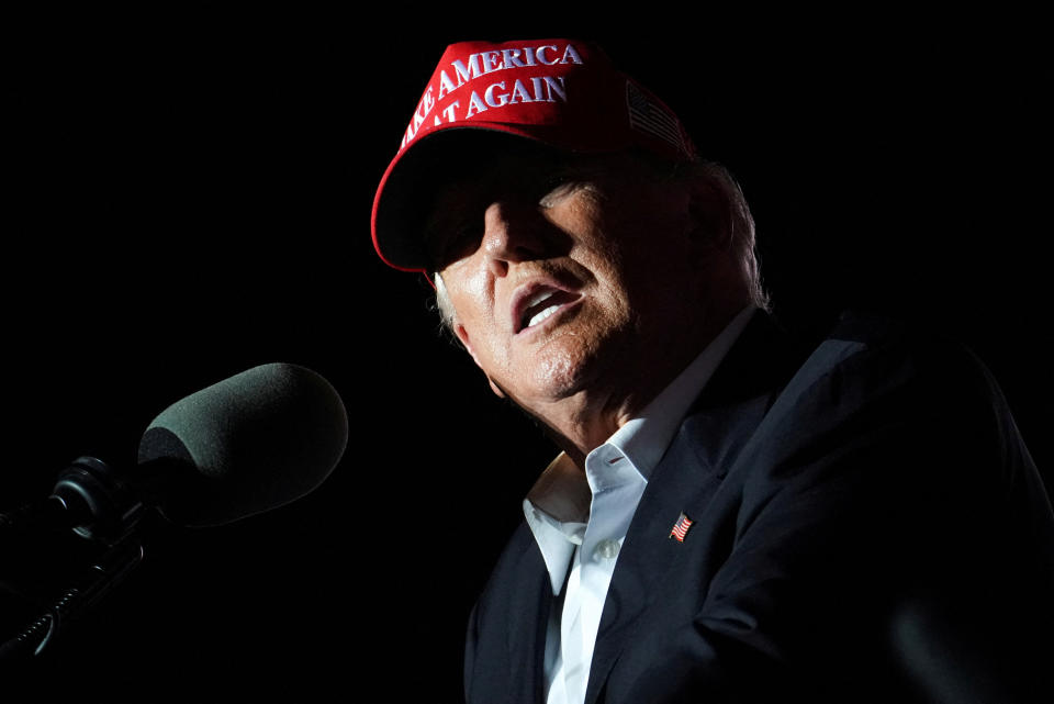 Donald Trump, wearing a red MAGA baseball cap, at the microphone. 