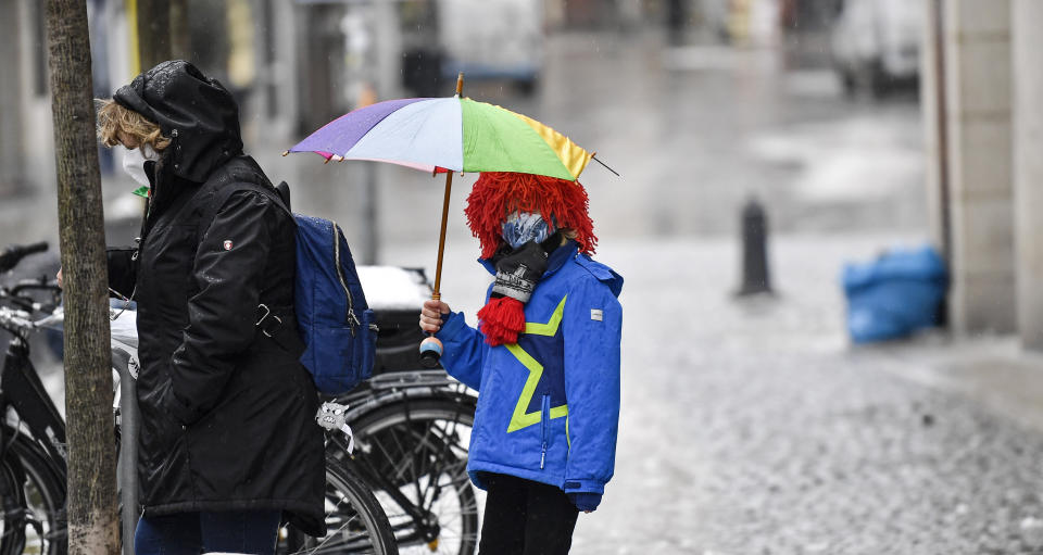 A young carnival reveller dressed as a clown holds an umbrella in the empty old town in Duesseldorf, Germany, Monday, Feb. 15, 2021. Because of the coronavirus pandemic the traditional; carnival parades are canceled but eight floats are pulled through the empty streets in Duesseldorf, where normally hundreds of thousands of people would celebrate the street carnival. (AP Photo/Martin Meissner)