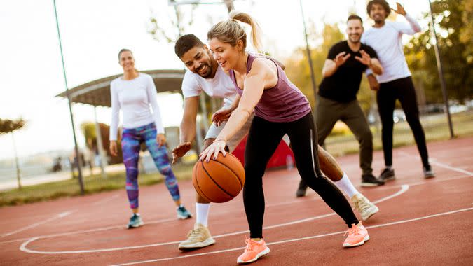 Group of multiracial young people   playing basketball  on court at outdoors.