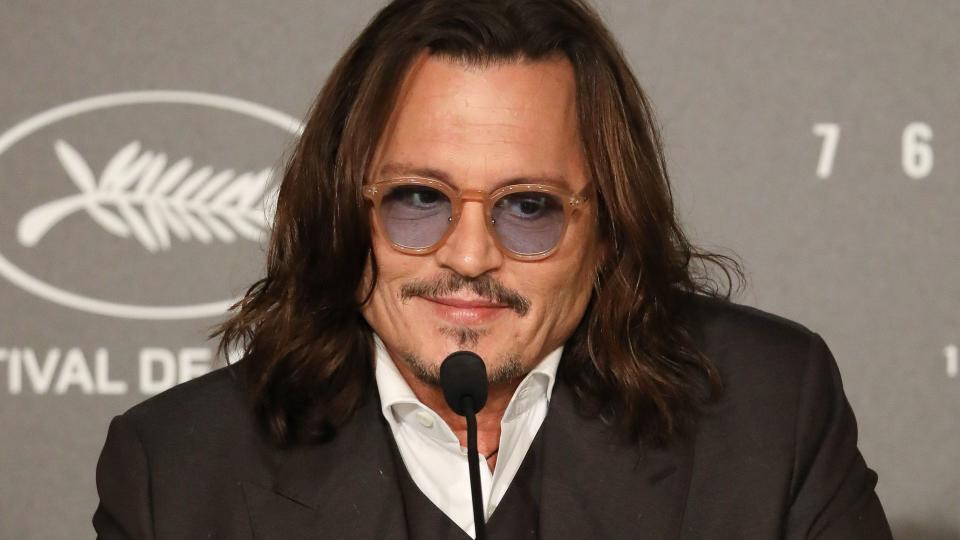 Johnny Depp smiling while sat at a press conference