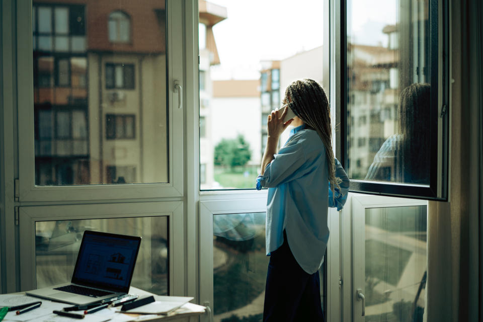 Woman standing by an open door, looking out, with a laptop on a desk nearby