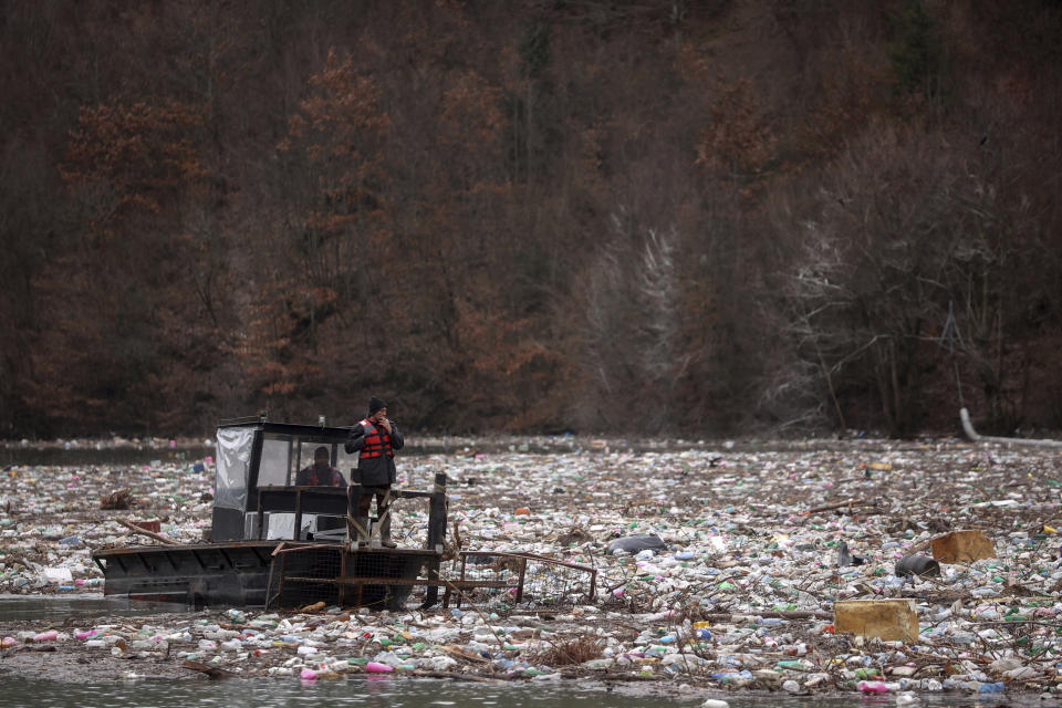 Utility company workers push the waste to the shore of Lim river near Priboj, Serbia, Monday, Jan. 30, 2023. Plastic bottles, wooden planks, rusty barrels and other garbage dumped in poorly regulated riverside landfills or directly into the rivers accumulated during high water season, behind a trash barrier in the Lim river in southwestern Serbia. (AP Photo/Armin Durgut)