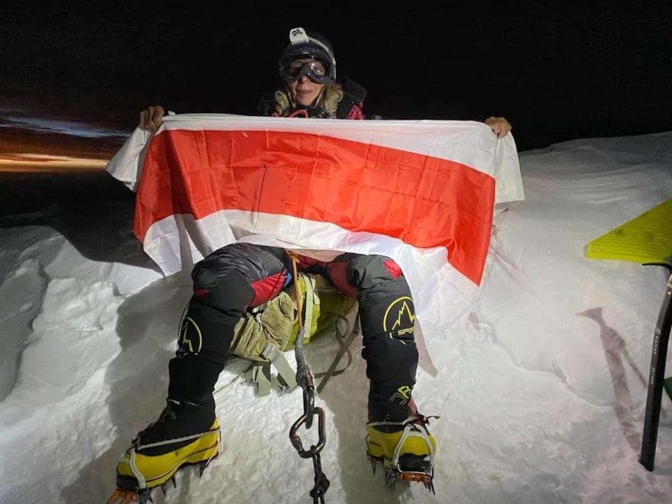 Belarusian-Canadian Liliya Ianovskaia holding a Belarusian national flag at the K2 peak in Pakistan on July 22. Ianovskaia, now 63, said she took up mountaineering at the age of 50.  (Submitted by Liliya Ianovskaia - image credit)