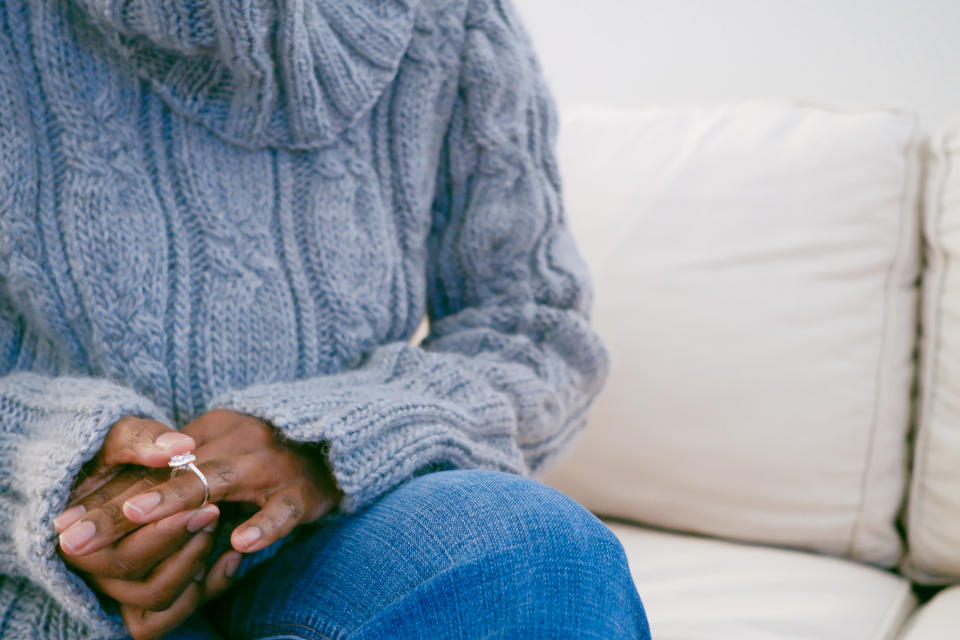 Person in a knitted sweater seated with an engagement ring on the finger, hinting at a romantic milestone