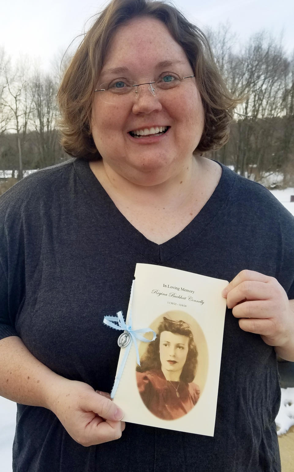 Julie Fry poses outside her home in Port Matilda, Pa., with a memorial booklet honoring her late grandmother Regina Connelly on Feb. 4, 2021. After Connrlly died of COVID-19 at her nursing home last December, there was no large church celebration of her life. Fry and her sister put together a “memory book” shared with family and friends. (Patricia C. Fry via AP)