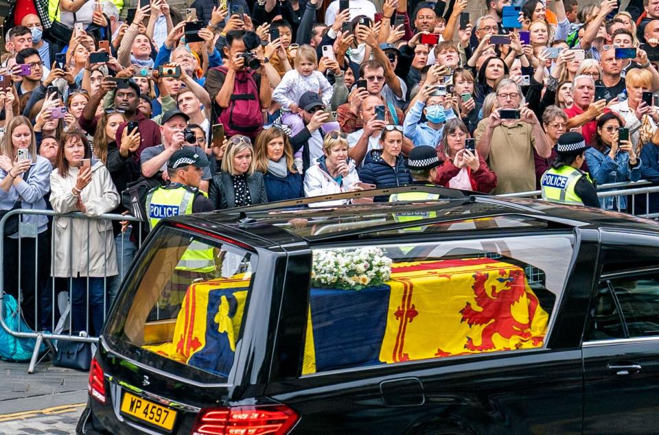 Members of the public gather to watch the hearse carrying the coffin of Queen Elizabeth II, draped in the Royal Standard of Scotland, as it is driven through Edinburgh towards the Palace of Holyroodhouse, on September 11, 2022. - The coffin carrying the body of Queen Elizabeth II left her beloved Balmoral Castle on Sunday, beginning a six-hour journey to the Scottish capital of Edinburgh. (Photo by Jane Barlow / POOL / AFP) (Photo by JANE BARLOW/POOL/AFP via Getty Images)