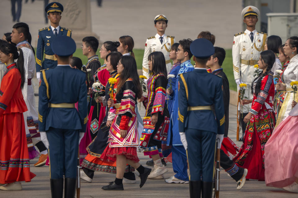 Participants in ethnic minority dress carry flowers as they walk during a ceremony to mark Martyr's Day at the Monument to the People's Heroes at Tiananmen Square in Beijing, Friday, Sept. 30, 2022. (AP Photo/Mark Schiefelbein)