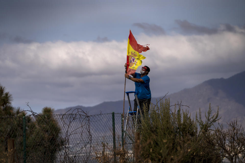 A resident fixes a Spanish flag on his courtyard while leaving his house stalked by the lava that advances towards the neighbourhood on the Canary island of La Palma, Spain, Friday, Oct. 29, 2021. An erupting volcano in the Spanish island of La Palma continued to emit vast amounts of magma, gases and ash, after days of intense seismic activity and more than five weeks since it erupted. (AP Photo/Emilio Morenatti)