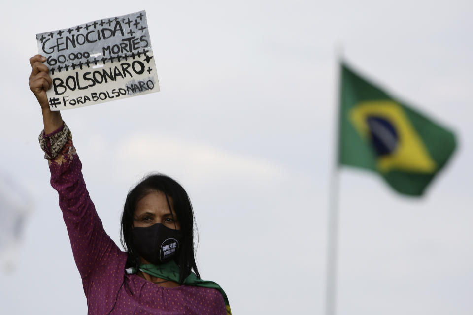 A women's movement activist holds a sign that reads in Portuguese "Genocide 60 thousand deaths, Bolsonaro out," during a protest against the government's inefficiency in the face of the new coronavirus pandemic and the ongoing police brutality against blacks, in front of the National Congress, in Brasilia, Brazil, Thursday, July 2, 2020. (AP Photo/Eraldo Peres)