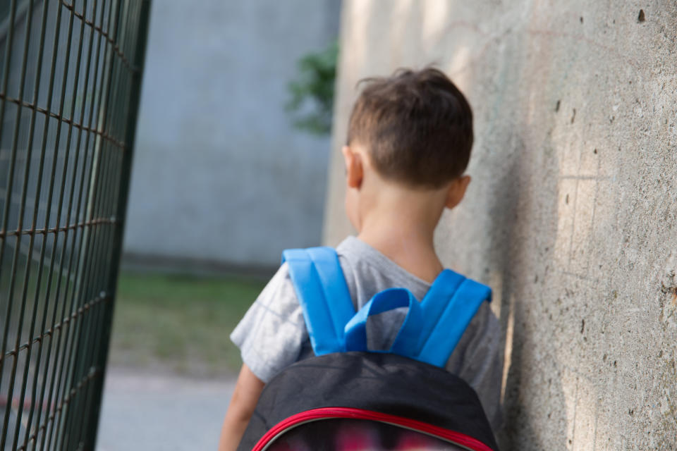 School boy with his back to the camera looking sad with a backpack