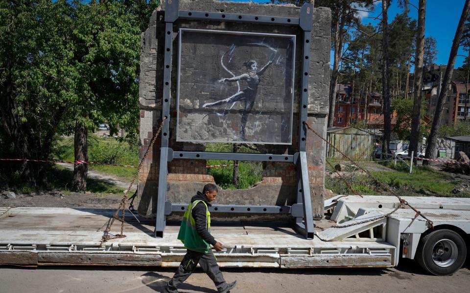 Artwork made by British street artist Banksy is seen on part of a wall of a building destroyed by fighting as the structure stands on a platform before it's presentation in the city park in Irpin, near Kyiv, Ukraine - Efrem Lukatsky/AP