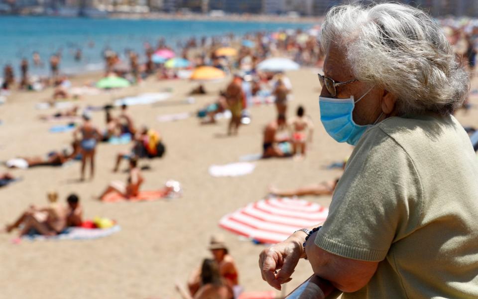  A woman wearing a face mask watches people sunbathing on the Las Canteras beach - Reuters 