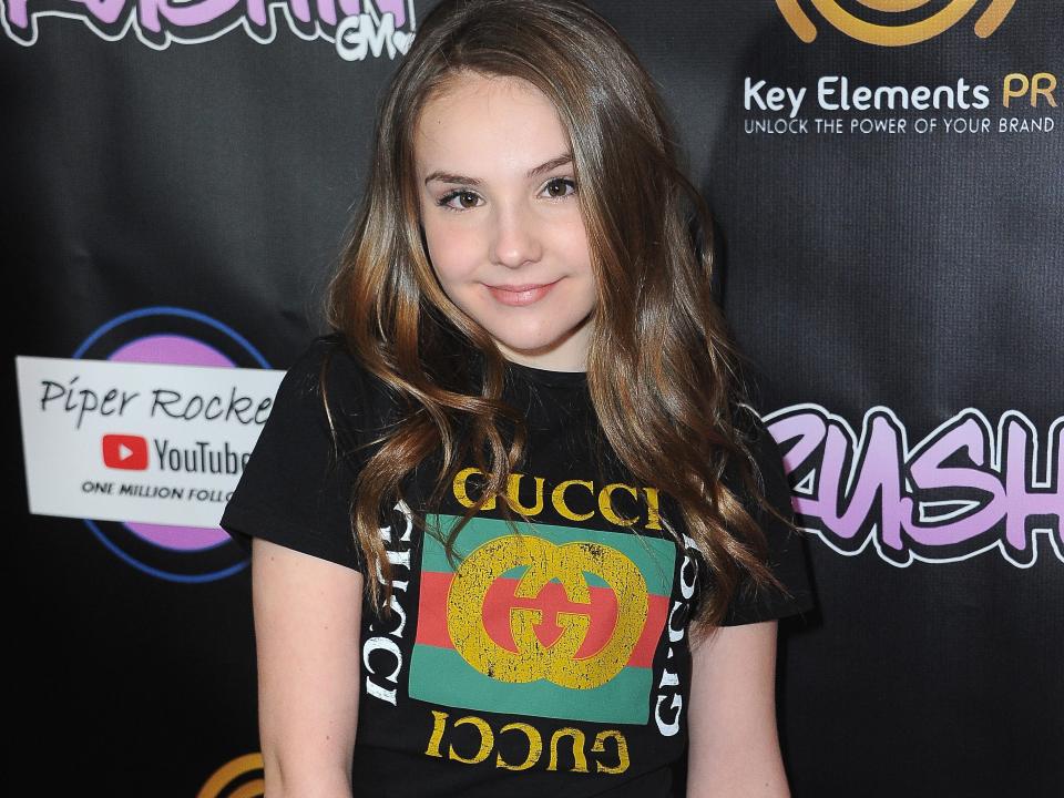 piper rockelle in a white skirt and gucci t-shirt standing on a red carpet; the bacvkground includes the word "crushin" as well as an illustration that reads "piper rockelle youtube one million subscribers"