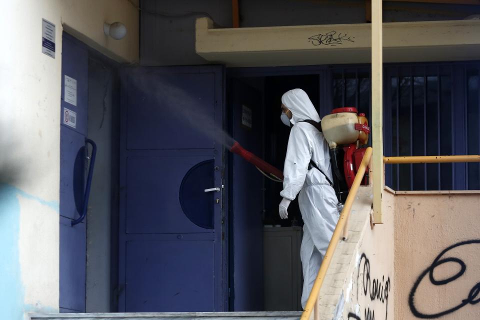 A worker wearing a protective suit sprays disinfectant at a high school in the northern city of Thessaloniki, Greece, on Thursday, Feb. 27, 2020. Greece's Health Minister Vassilis Kikilias said all carnival events in Greece would be suspended as a precautionary measure. (AP Photo/Giannis Papanikos)