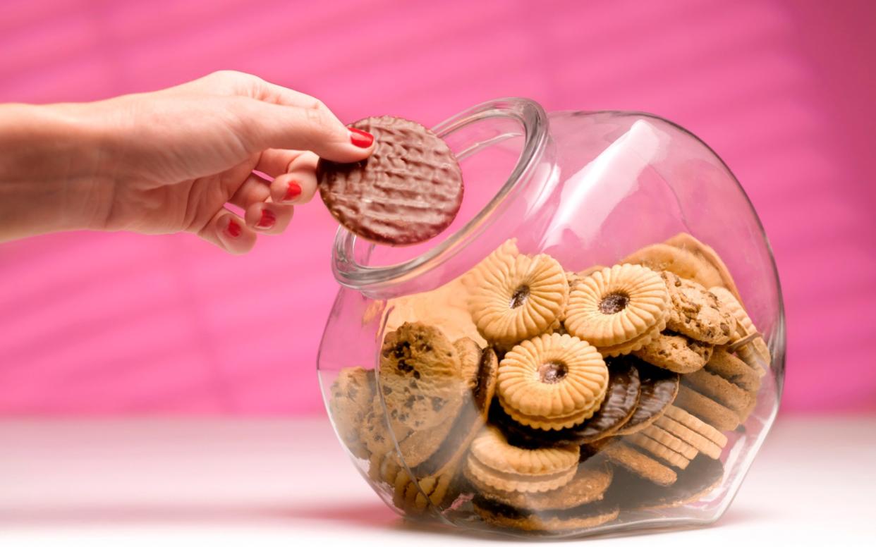 Woman sneaks a biscuit treat from the cookie jar - Peter Dazeley/The Image Bank RF