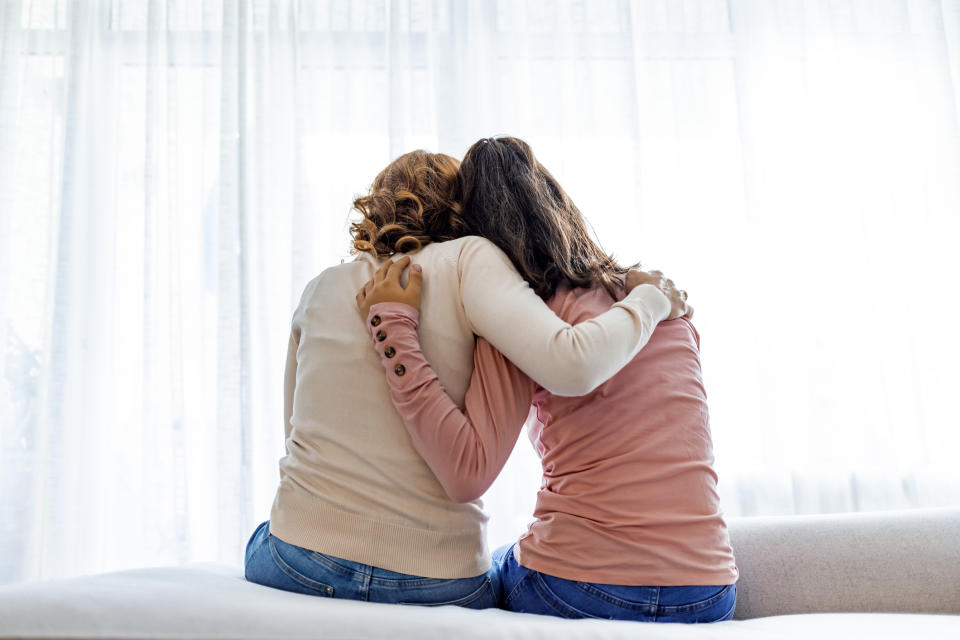 Two people sitting closely, embracing, looking out a window, conveying a sense of support and companionship