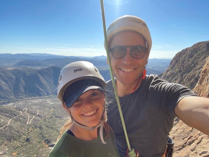 A selfie of a smiling couple high on a California rock climb-the desert and the sky behind them.