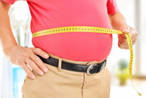 A man holding a tape measure around his stomach.