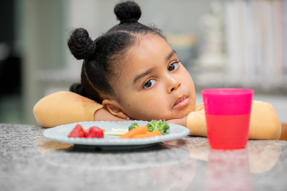 Little girl who is a picky eater and refuses to eat healthy meal sits at a kitchen counter. (Photo via Getty Images)