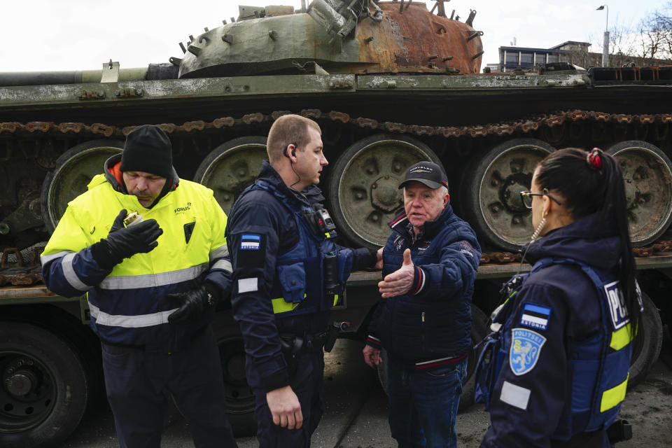 A security guard, left, blows out a candle as police officers talk with a man who placed it next to a destroyed Russian T-72B3 tank installed as a symbol of the Russia Ukraine war to mark the first anniversary of Russia's full-scale invasion of Ukraine, in Freedom Square in Tallinn, Estonia, Wednesday, March 1, 2023. (AP Photo/Pavel Golovkin)