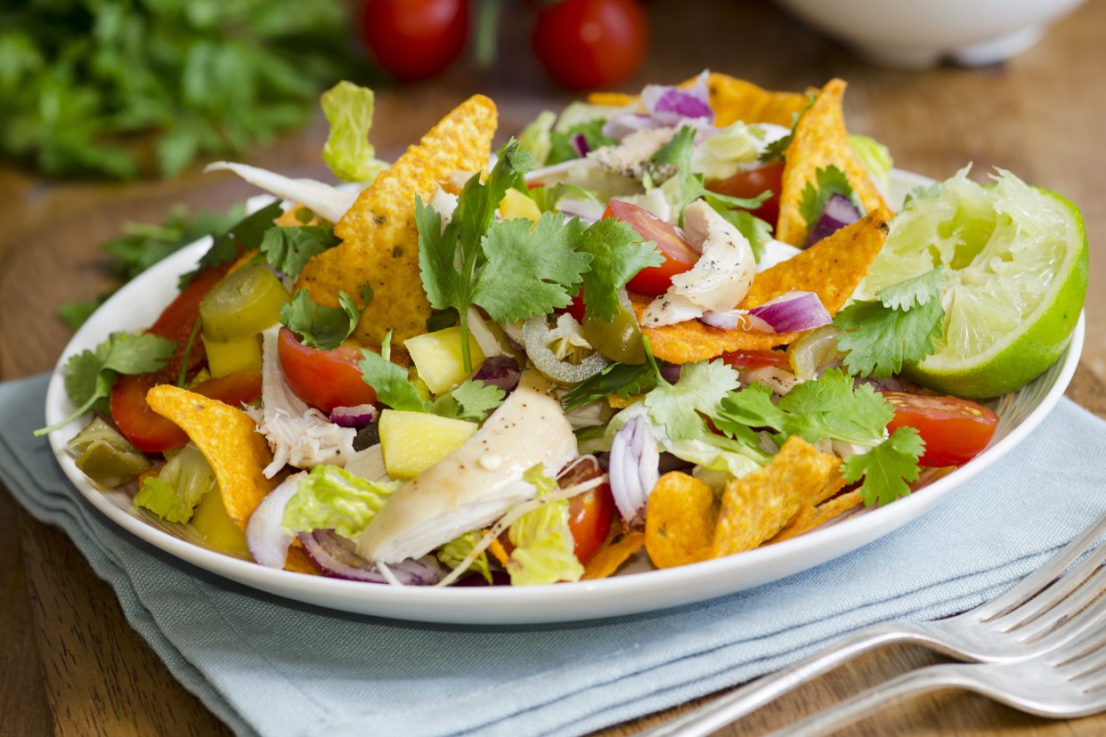 Spicy chicken mango jalapeño salad in an oval white porcelain plate on a light blue napkin with two forks on a table with ingredients blurred in the background