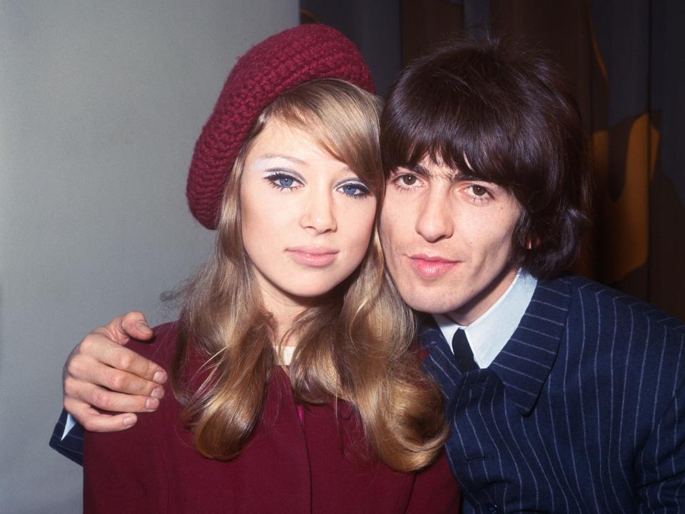 Pattie in a burgundy top and beret and George hugging her in a blue suit.