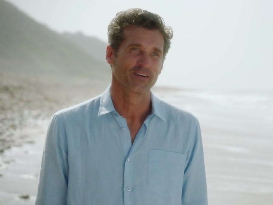 Patrick Dempsey as Derek on Greys Anatomy on a beach wearing a blue shirt