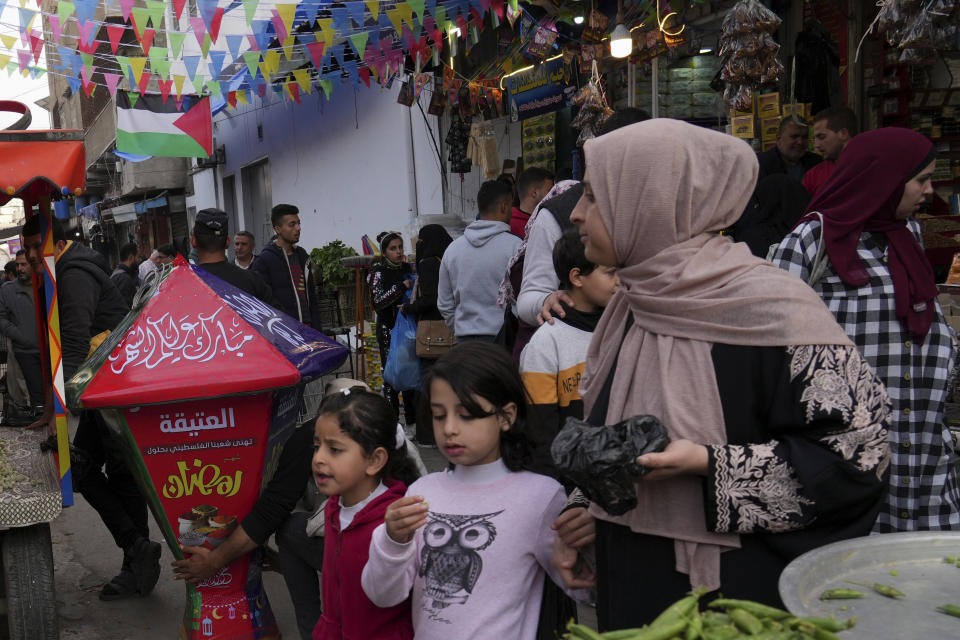 A woman and her daughters walk near a traditional lantern while they shop for the Muslim holy month of Ramadan, at al-Zawya traditional market in Gaza City, Thursday, March 31, 2022. As Ramadan begins with the new moon next week, Muslims around the world are trying to maintain their religious rituals of Islamic holiest month. (AP Photo/Adel Hana)