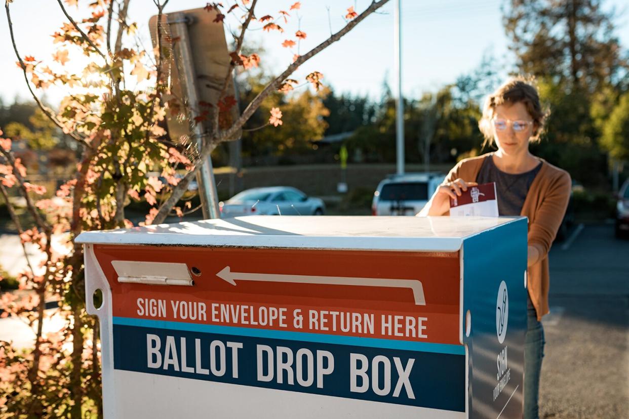 A woman deposits her vote in a sealed envelope into an official voting ballot box in Washington state, USA.