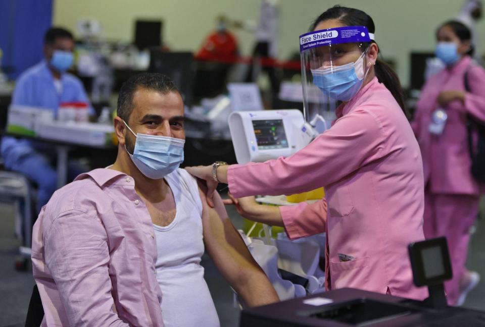 man in a mask getting covid-19 vaccine administered by woman in mask, shield