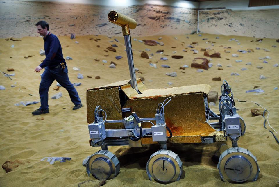 Engineer Ben Nye walks past a robotic vehicle on the 'Mars Yard Test Area', a testing ground for the robotic vehicles of the European Space Agency’s ExoMars program scheduled for 2018, in Stevenage, England, Thursday, March 27, 2014. It looks like a giant sandbox - except the sand has a reddish tint and the “toys” on display are very expensive prototypes designed to withstand the rigors of landing on Mars. The scientists here work on the development of the autonomous navigation capabilities of the vehicle, so by being in communication with controllers on earth twice a day, will be able to use the transmitted information to navigate to new destinations on Mars. (AP Photo/Lefteris Pitarakis)