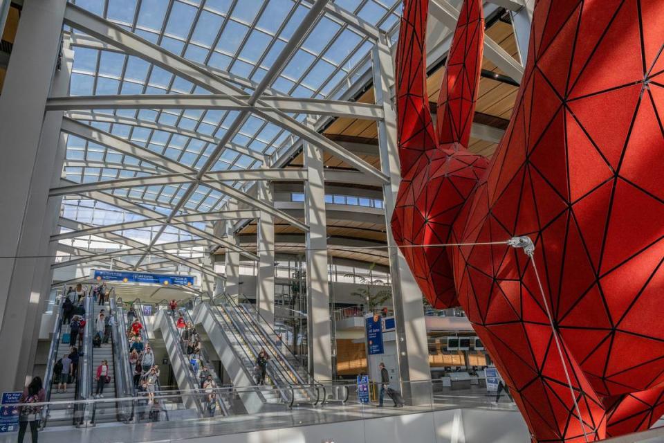 Travelers descend escalators under the watchful eye of “Leap,” the red rabbit sculpture by Lawrence Argent, as they make their way toward baggage claim in Sacramento International Airport’s Terminal B on Nov. 22, 2023, the day before Thanksgiving.