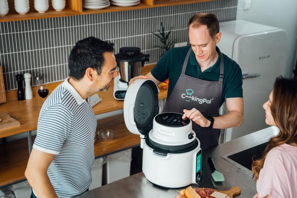 A person adjusts settings on CookingPal&#39;s Pronto pressure cooker as two others look on.