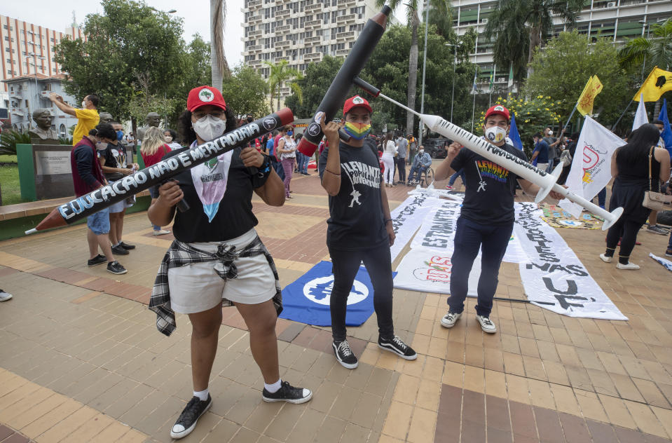 Demonstrators holding fake guns shaped like pencils, and a syringe, attend a protest against Brazilian President Jair Bolsonaro and his handling of the pandemic and economic policies protesters say harm the interests of the poor and working class, in Cuiaba, Brazil, Saturday, June 19, 2021. (AP Photo/Andre Penner)