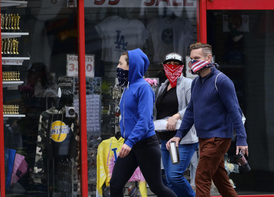 Pedestrians wearing masks during the coronavirus outbreak walk along a deserted Hollywood Boulevard, Sunday, April 5, 2020, in the Hollywood section of Los Angeles. The coronavirus mainly is spread though coughs and sneezes. The new coronavirus causes mild or moderate symptoms for most people, but for some, especially older adults and people with existing health problems, it can cause more severe illness or death. (AP Photo/Richard Vogel)