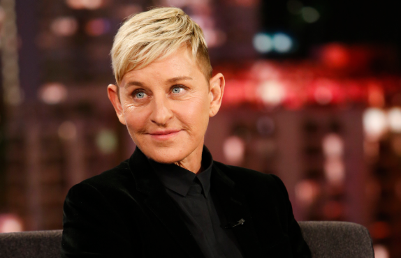 Ellen Degeneres smiles as she sits down and wears jeans and black blazer