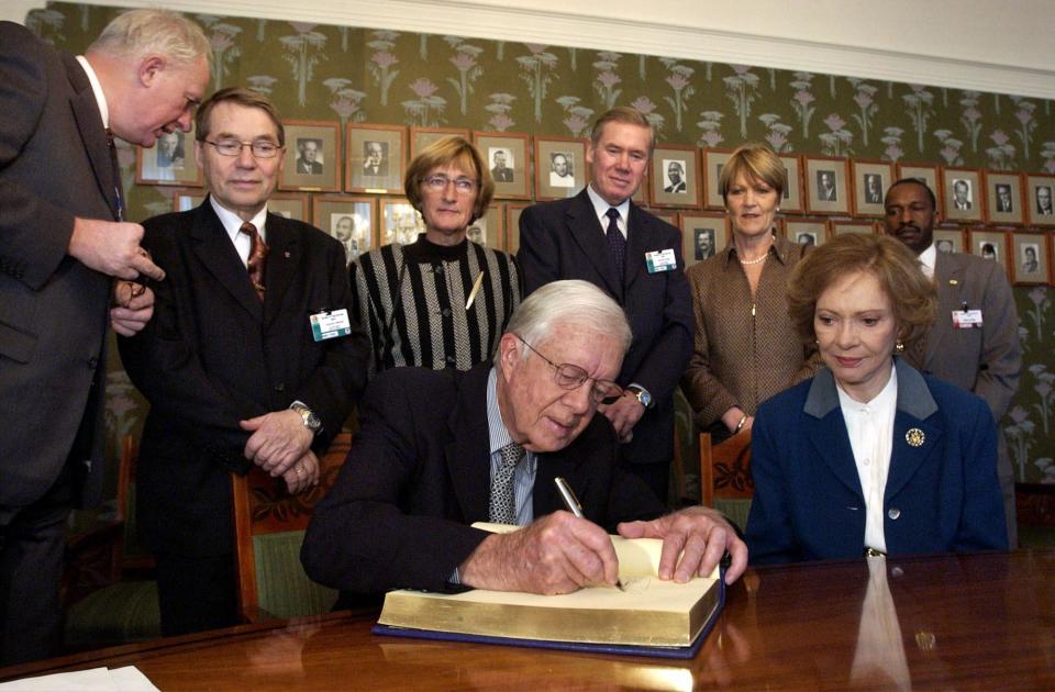 Nobel Peace Prize winner Jimmy Carter signs the guestbook in the Nobel Institute in Oslo, Norway, on Dec. 9, 2002, next to his wife Rosalynn, as members of the Norwegian Nobel Committee look on. / Credit: -/POOL/AFP via Getty Images