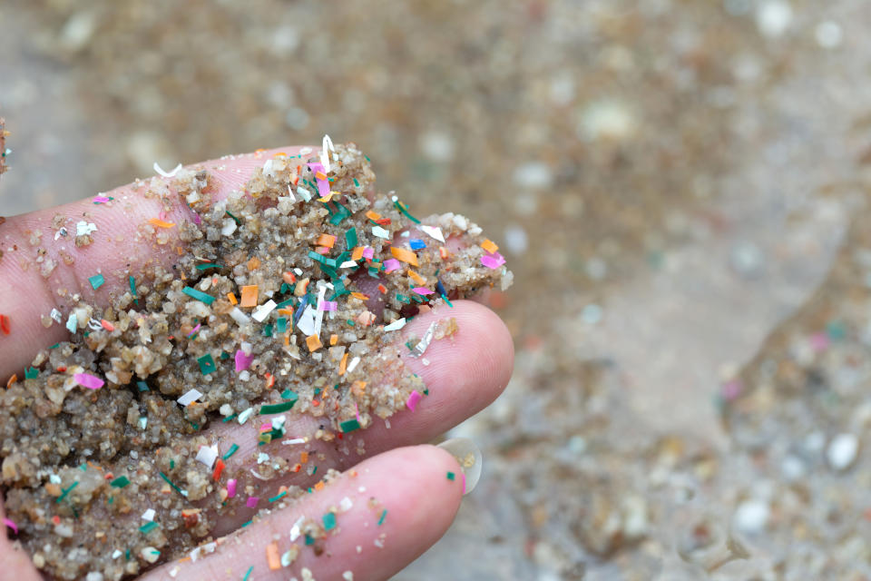 Close-up side shot of hands shows microplastic waste contaminated with the seaside sand. Microplastics are contaminated in the sea. Concept of water pollution and global warming.