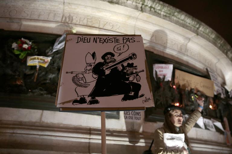 Un letrero con una caricatura religiosa que dice &quot;Dios no existe, si!&quot; realizada por el difunto dibujante francés Cabu es expuesta bajo la estatua de la plaza de la República en París, el 7 de enero de 2015, tras el mortal ataque contra el semanario Charlie Hebdo