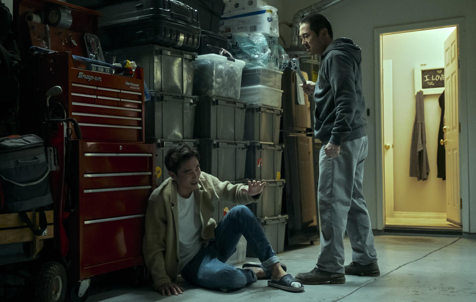 A man holding a wrench hovers menacingly over another man sitting on the floor of a storage room; still from "Beef"