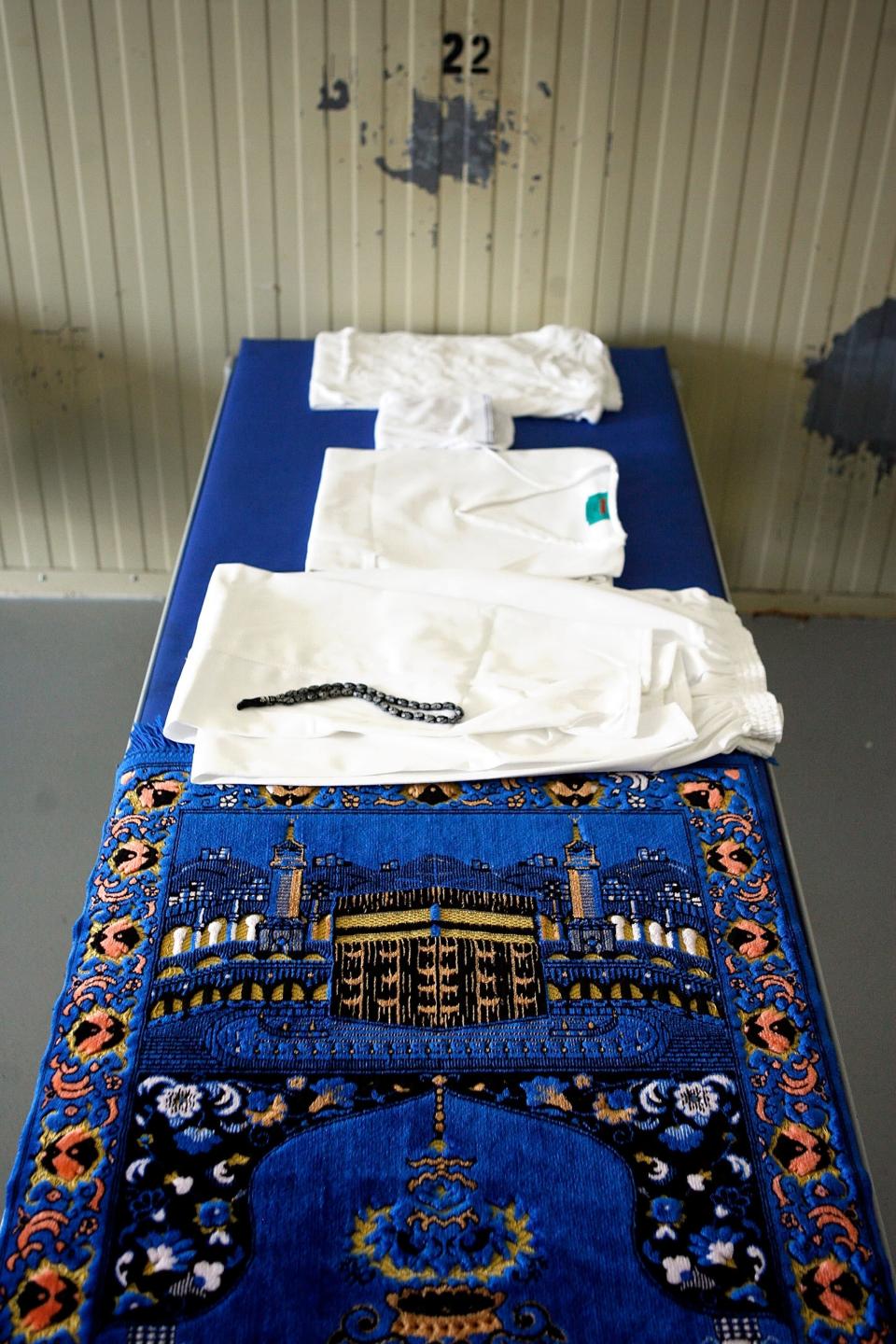 GUANTANAMO BAY, CUBA - OCTOBER 2:  (IMAGE REVIEWED BY U.S. MILITARY PRIOR TO TRANSMISSION) White clothing, prayer beads and a prayer rug, with an image of Mecca, sits on a bed for detainees who exhibit good behavior inside Camp 4 at the detention facility at the U.S. Naval Station October 2, 2007 in Guantanamo Bay, Cuba. About 340 "unlawful enemy combatants" captured since the September 11, 2001 attacks on the United States continue to be held at the facility.  (Photo by Chip Somodevilla/Getty Images)