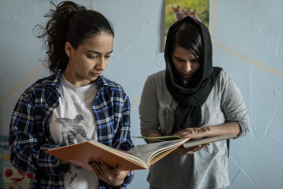 18-year-old Andisheh, left, and her 23-year-old sister Zohal, two Afghan asylum seekers, read books in the library of a refugee shelter, in Eichsfeld, Germany, Wednesday, April 24, 2024. Across Germany, cities and counties are introducing new payment cards for asylum-seekers. The new rule, which was passed by parliament last month, calls for the migrants to receive their benefits on a card that can be used for payments in local shops and services. (AP Photo/Ebrahim Noroozi)
