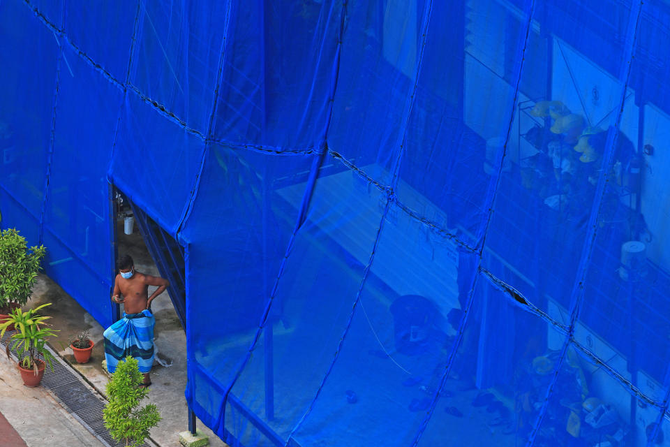 SINGAPORE - MAY 28:  A migrant worker stands outside his makeshift dormitory room, fitted with exterior netting, at a stalled construction site on May 28, 2020 in Singapore. Singapore is set to ease the partial lockdown measures against the coronavirus (COVID-19) pandemic after 1 June in three phases to resume activities safely after it sees a decline in the new infection cases within the community. Building contractors will be allowed to gradually resume operations from June 2, with  safe distancing measures in place, such as implementing contract tracing at worksites and avoiding cross deployment of workers.  (Photo by Suhaimi Abdullah/Getty Images)