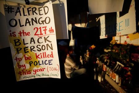 A sign hangs in protest as a woman prays at a makeshift memorial after the death of Alfred Olango, who was shot by El Cajon police Tuesday, at the parking lot where he was shot in El Cajon, California, U.S. September 29, 2016. REUTERS/Patrick T. Fallon
