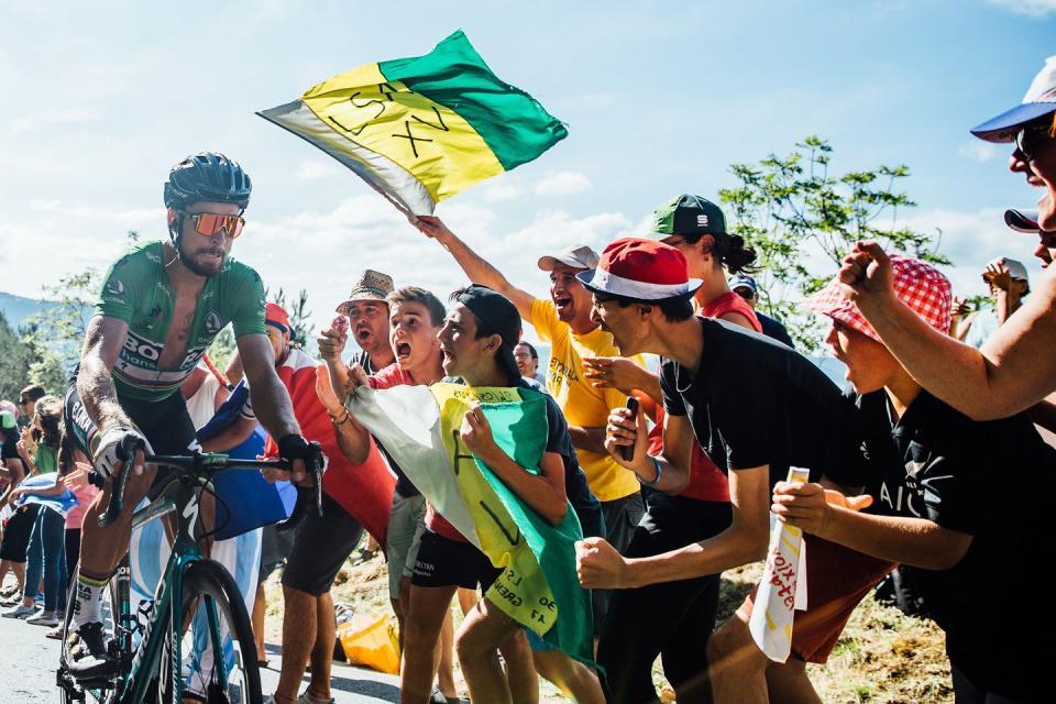 a group of fans holding a flag and cheering as sagan climbs part them