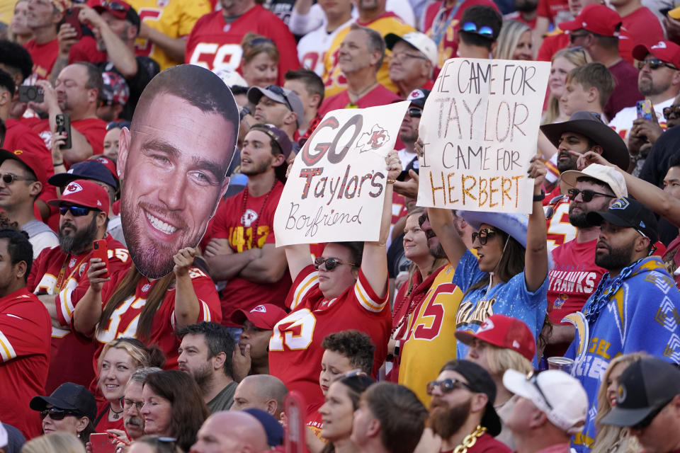 Fans hold sighs referring to Kansas City Chiefs tight end Travis Kelce (87) and Taylor Swift during the first half of an NFL football game between the Kansas City Chiefs and the Los Angeles Chargers Sunday, Oct. 22, 2023, in Kansas City, Mo. (AP Photo/Ed Zurga)
