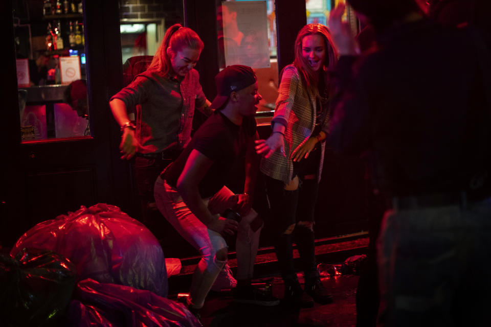 Late-night drinkers in Soho dance on the street in the early hours of Sunday, July 5, 2020, in London, as coronavirus lockdown restrictions eased across the country. England embarked on perhaps its biggest lockdown easing yet as pubs and restaurants reopened for the first time in more than three months. (Victoria Jones/PA via AP)