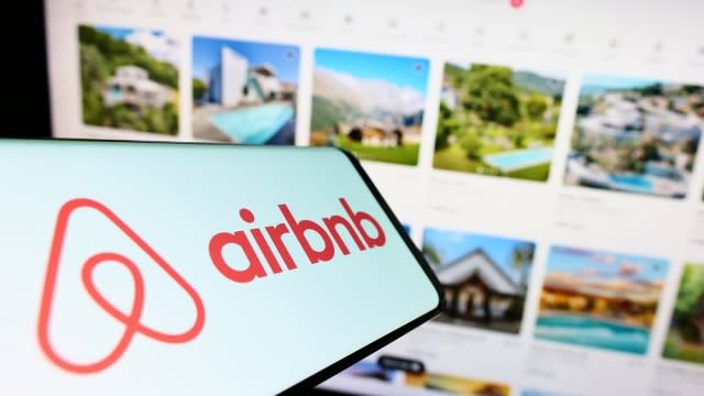 Smartphone with logo of Airbnb on screen in front of the business website.