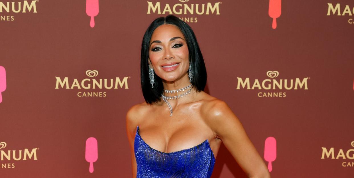 nicole scherzinger wearing a dark blue strapless gown with diamond earrings and a diamond necklace, smiling for the camera at a red carpet event