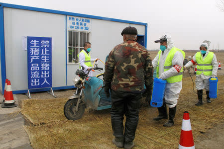 Workers in protective suits disinfect a vehicle at a checkpoint on a road leading to a farm owned by Hebei Dawu Group where African swine fever was detected, in Xushui district of Baoding, Hebei province, China February 26, 2019. REUTERS/Hallie Gu